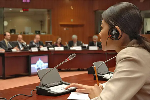 Interpreters need clean microphone audio, preparation material and an appropriate working position. Professional conference interpreter using a console during simultaneous interpretation